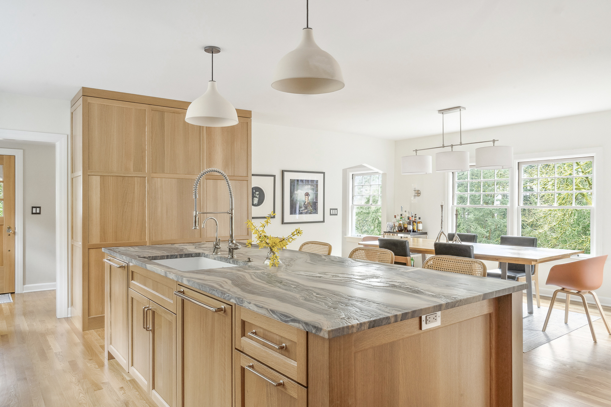 Island with leathered granite counter and sink, open view through to dining room with large windows, Arlington Heights Remodel by Tweto Architecture