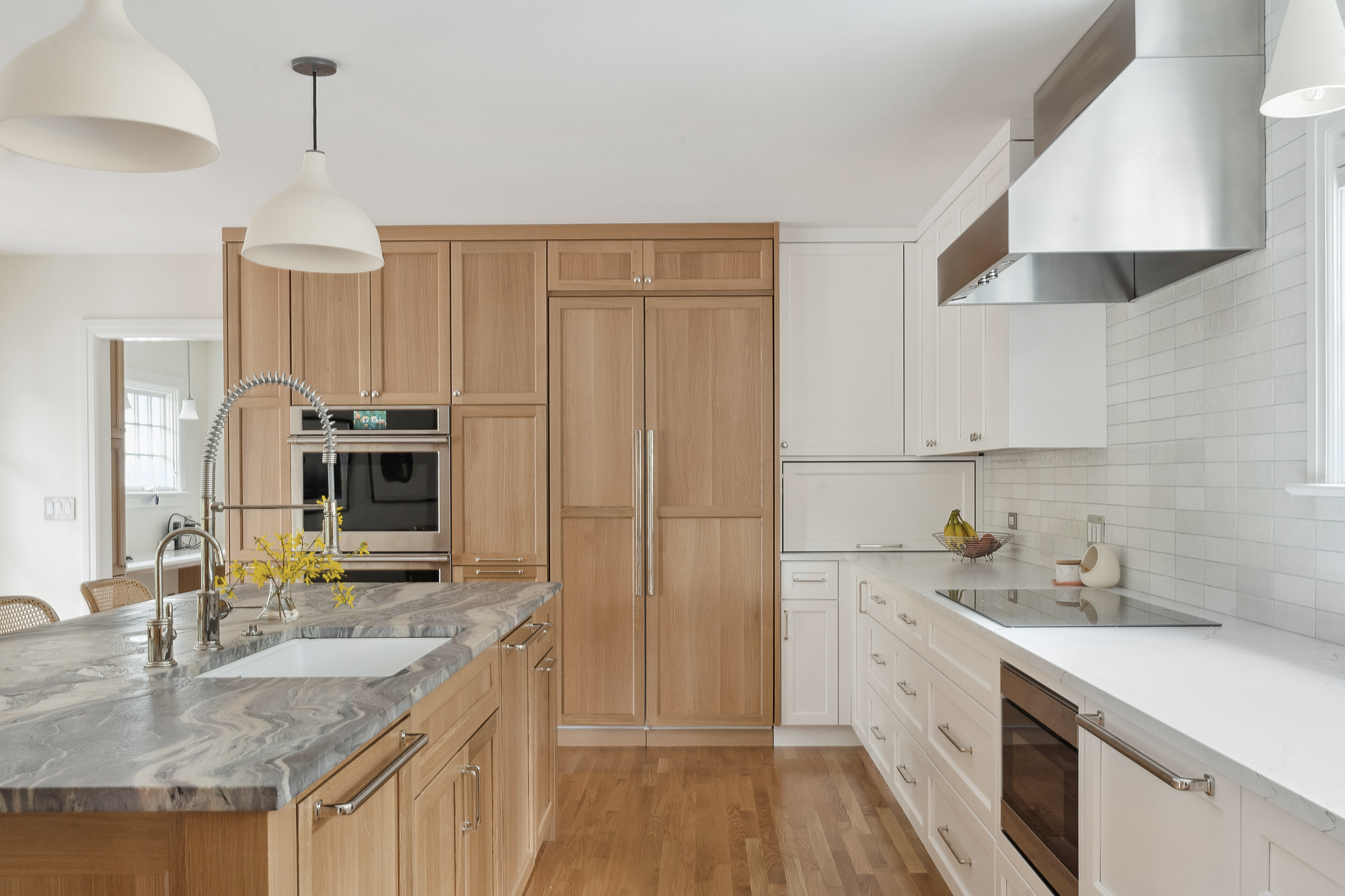 Tall oak storage wall with integrated double oven and panel-front refrigerator, white perimeter cabinets and island in foreground, Arlington Heights Remodel by Tweto Architecture