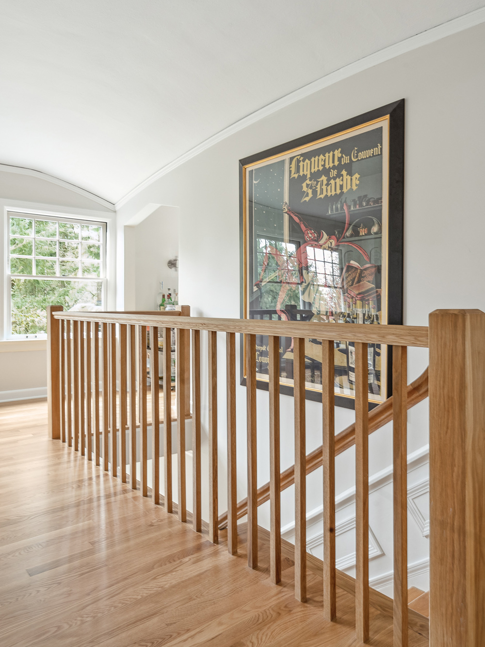 New white oak stair railing with square balusters at main floor landing, large vintage poster on wall beyond, Arlington Heights Remodel by Tweto Architecture