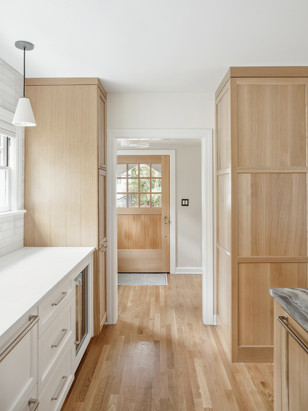 Narrow view between oak storage cabinets toward exterior door with arched transom window, Arlington Heights Remodel by Tweto Architecture
