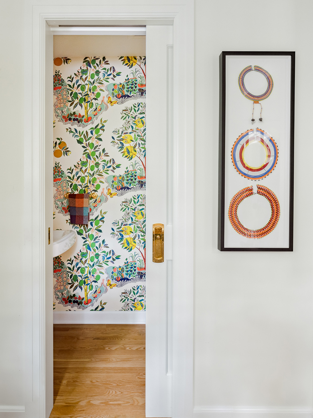 New half bath viewed through doorway, colorful botanical wallpaper and pedestal sink, Arlington Heights Remodel by Tweto Architecture
