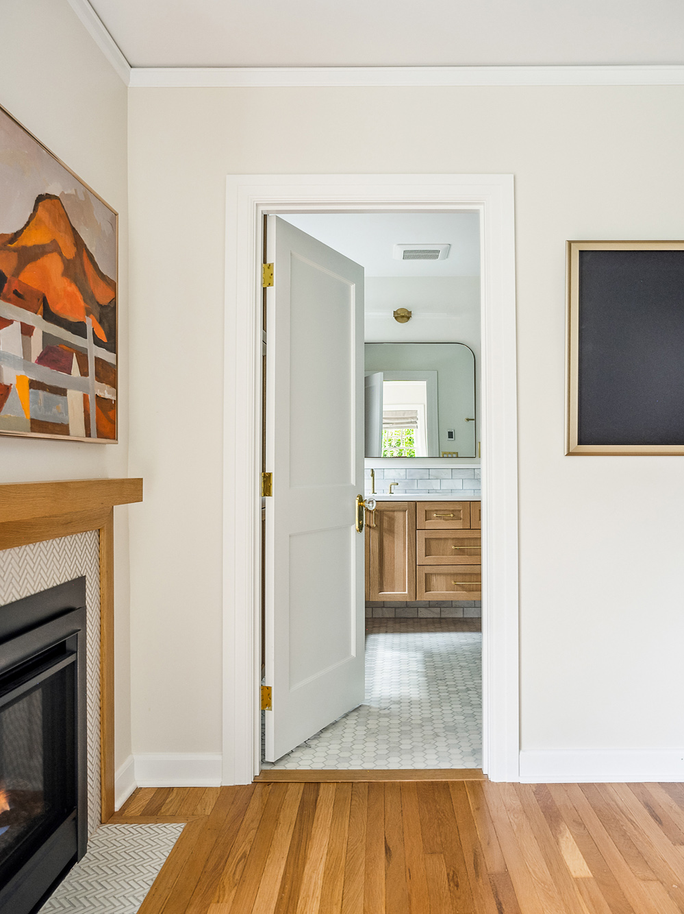 View from primary bedroom past gas fireplace through open door into primary bathroom with oak vanity beyond, Arlington Heights Remodel by Tweto Architecture