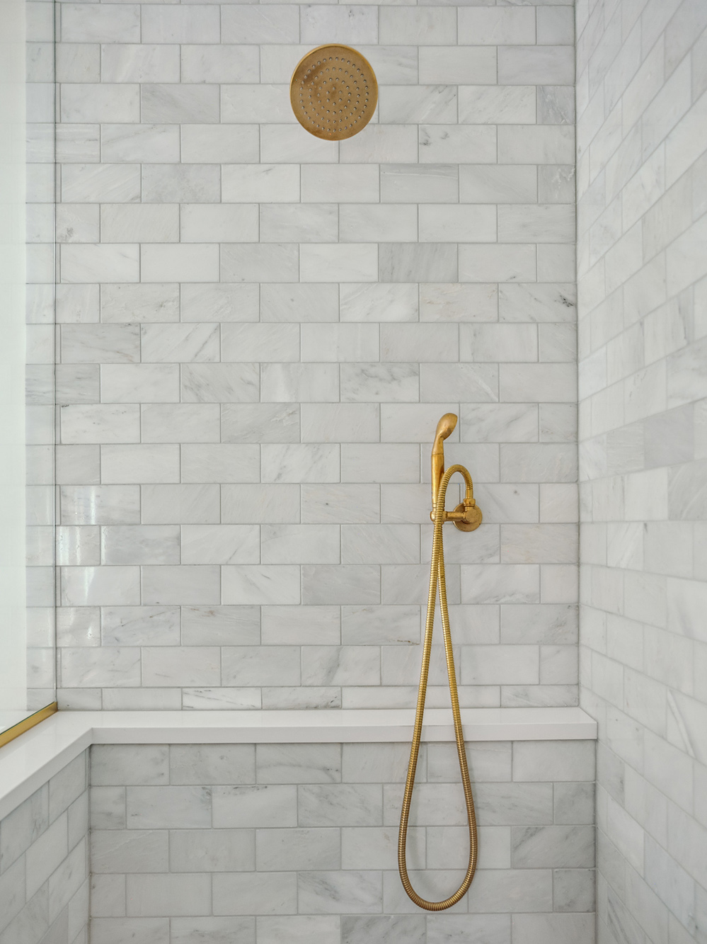 Primary shower interior with marble subway tile walls, built-in bench seat, and brass rain head and handheld fixtures, Arlington Heights Remodel by Tweto Architecture