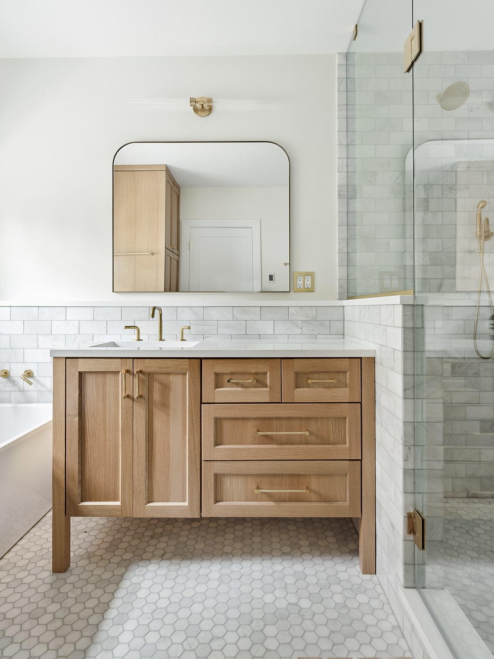 Custom white oak vanity with brass fixtures and arched mirror, marble tile wainscoting and hexagonal floor tile, Arlington Heights Remodel by Tweto Architecture