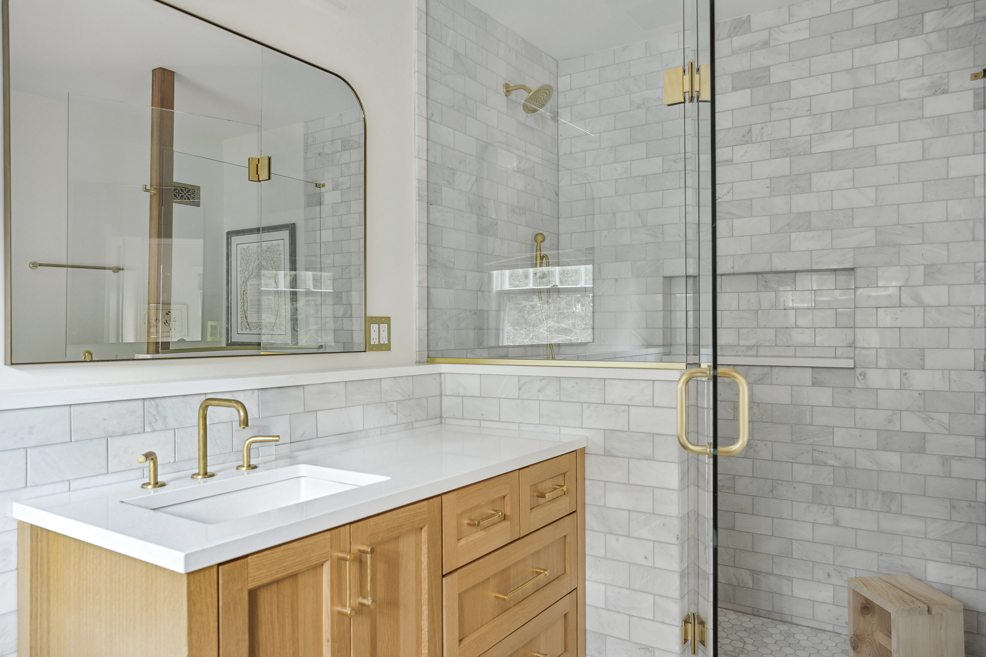 Primary bathroom with marble subway tile shower and glass enclosure, oak vanity with brass fixtures and arched mirror, Arlington Heights Remodel by Tweto Architecture