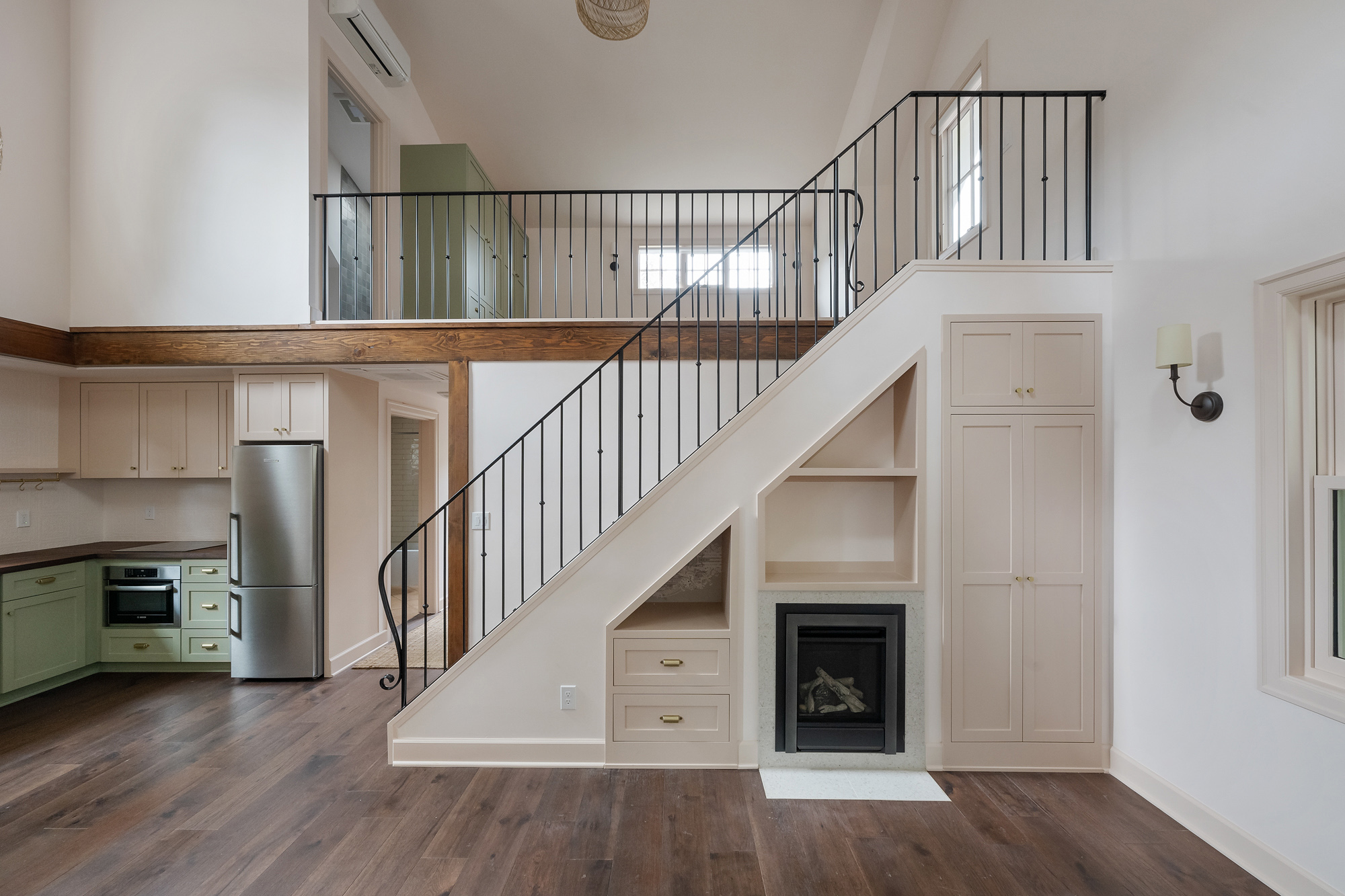 Stair with painted steel railing, built-in storage and fireplace insert below, and loft with exposed wood beam above, Buckman ADU SE Portland by Tweto Architecture
