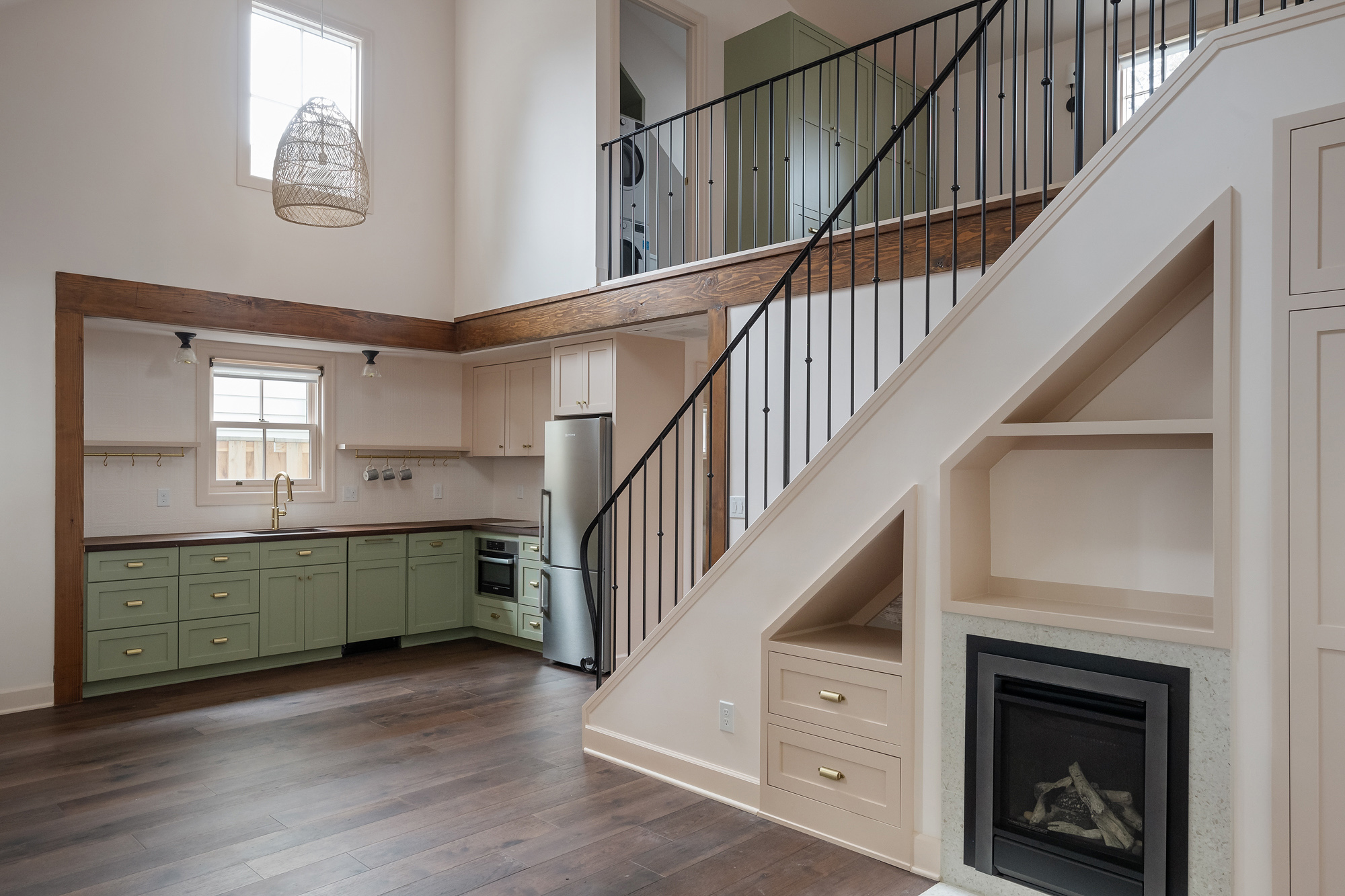 Green lower kitchen cabinets with walnut countertop and stair with painted steel railing beyond, Buckman ADU SE Portland by Tweto Architecture