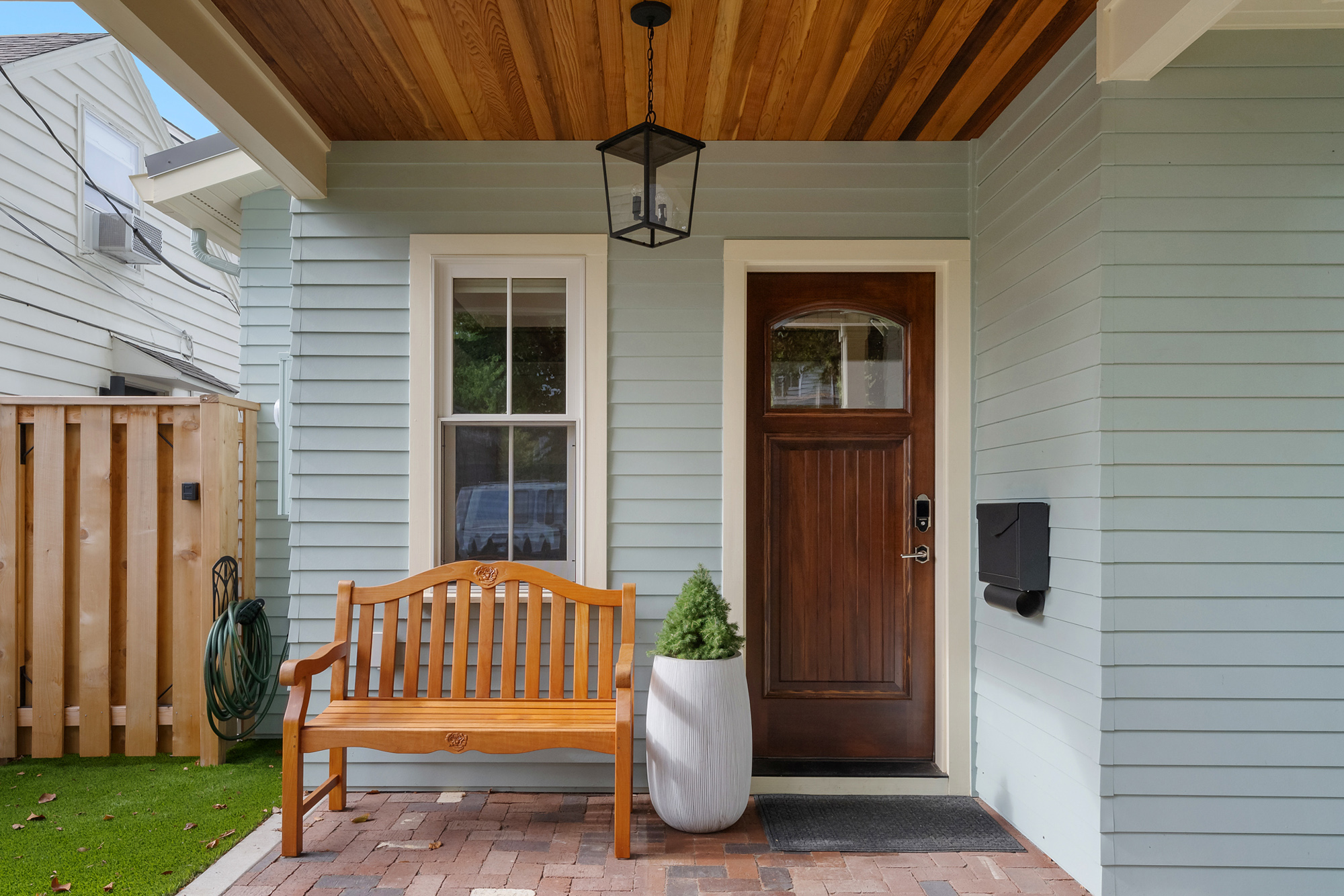 Buckman ADU covered front porch with wood-plank ceiling, pendant lantern, wood bench, and arched wood front door, SE Portland by Tweto Architecture