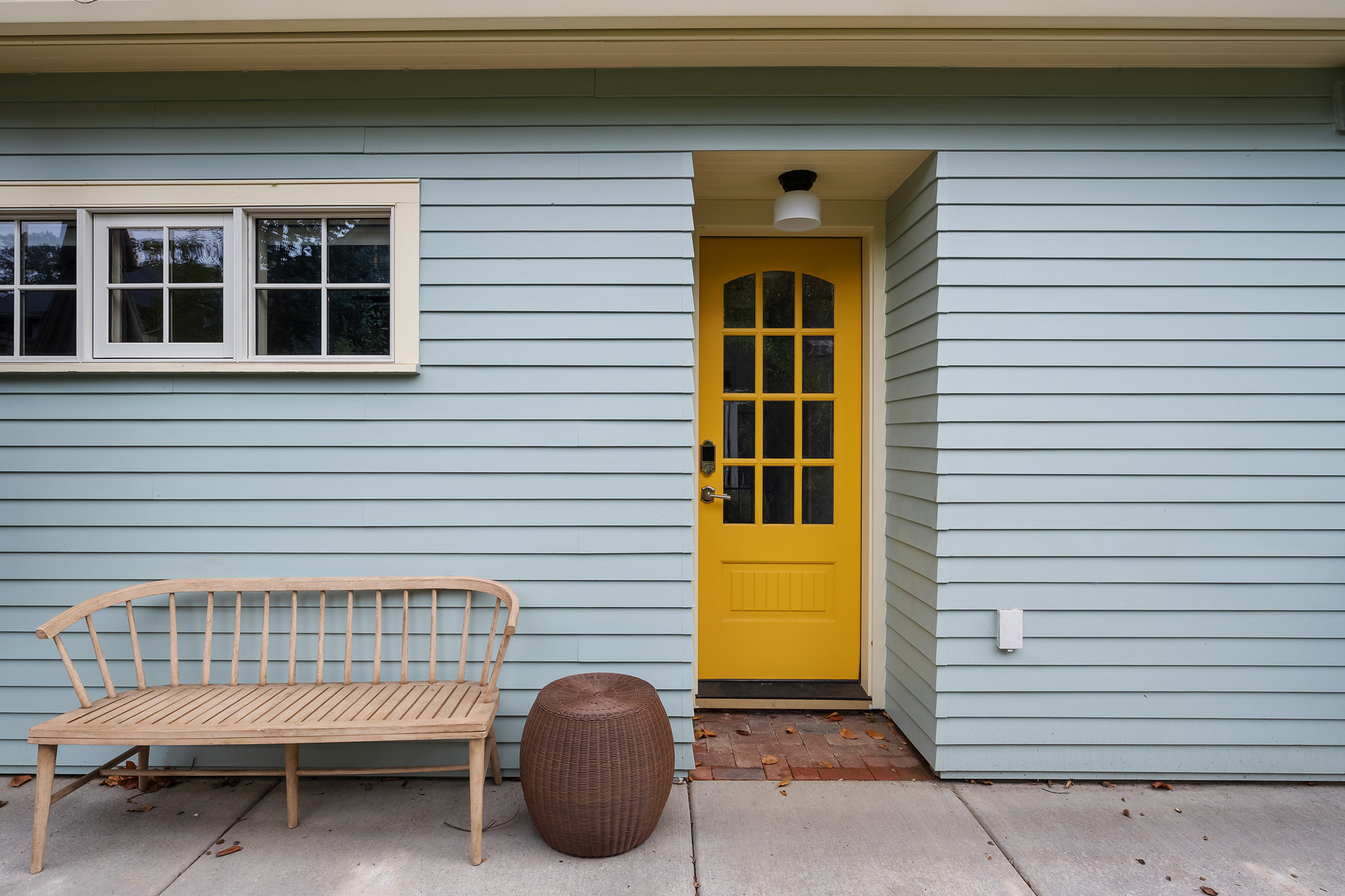 Rear exterior of the Buckman ADU with blue-green siding, yellow back door, and a bench at the entry to the daughter's yard, SE Portland by Tweto Architecture