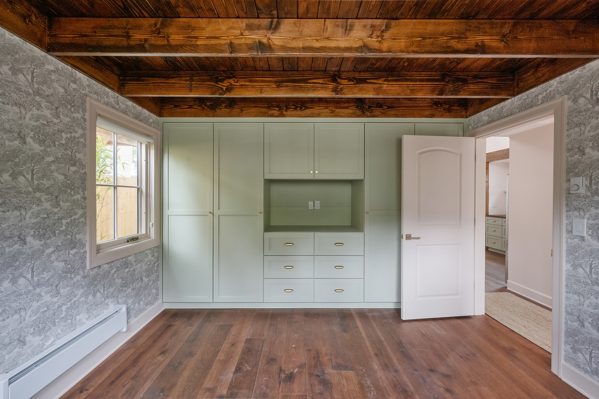 Floor-to-ceiling built-in wardrobe with drawers in the main-floor bedroom, exposed wood beam ceiling and toile wallpaper, Buckman ADU SE Portland by Tweto Architecture