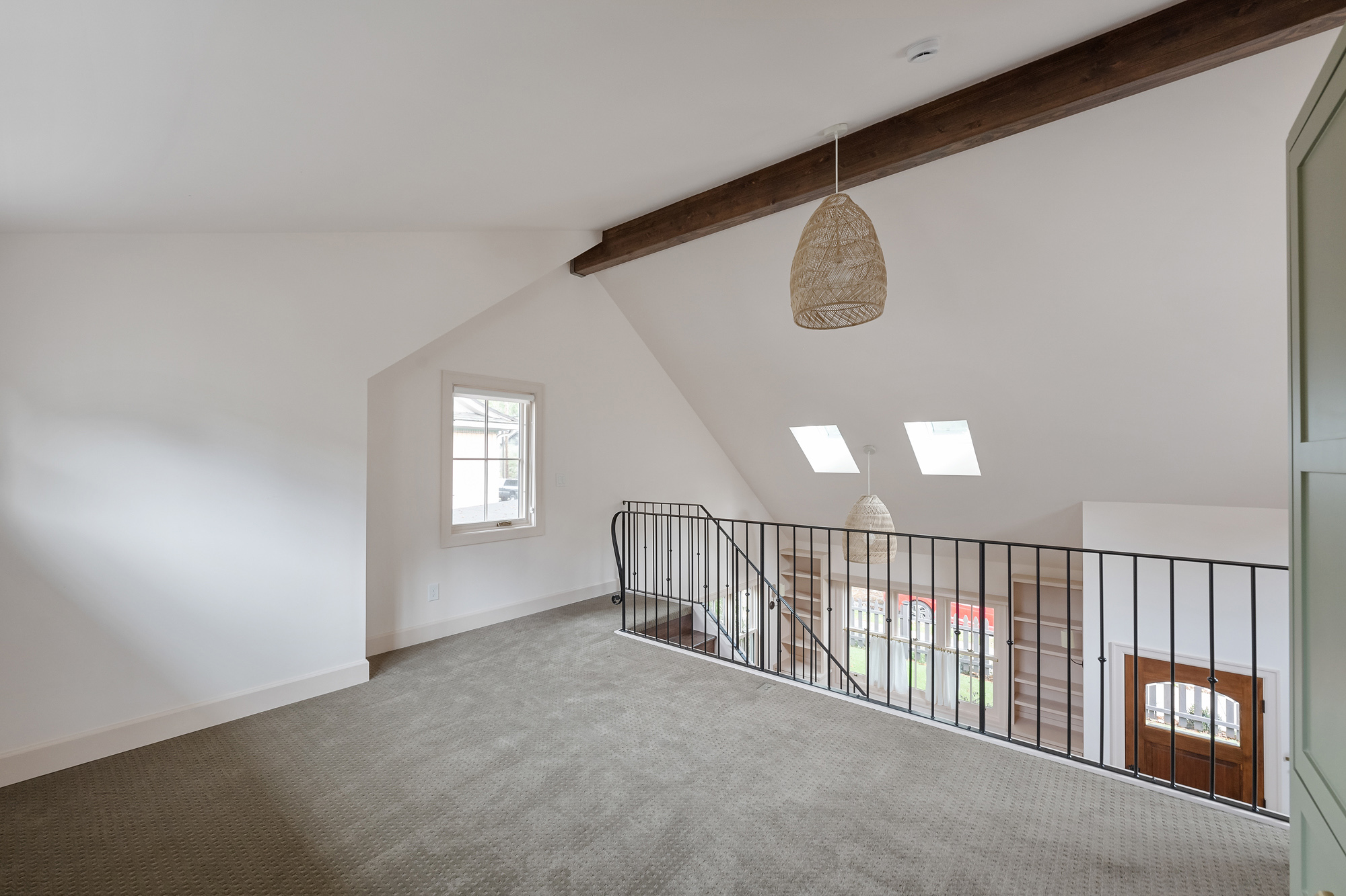 Loft bedroom with sloped ceiling, skylights, painted steel railing at the landing, and view down to the entry and built-in shelves below, Buckman ADU SE Portland by Tweto Architecture