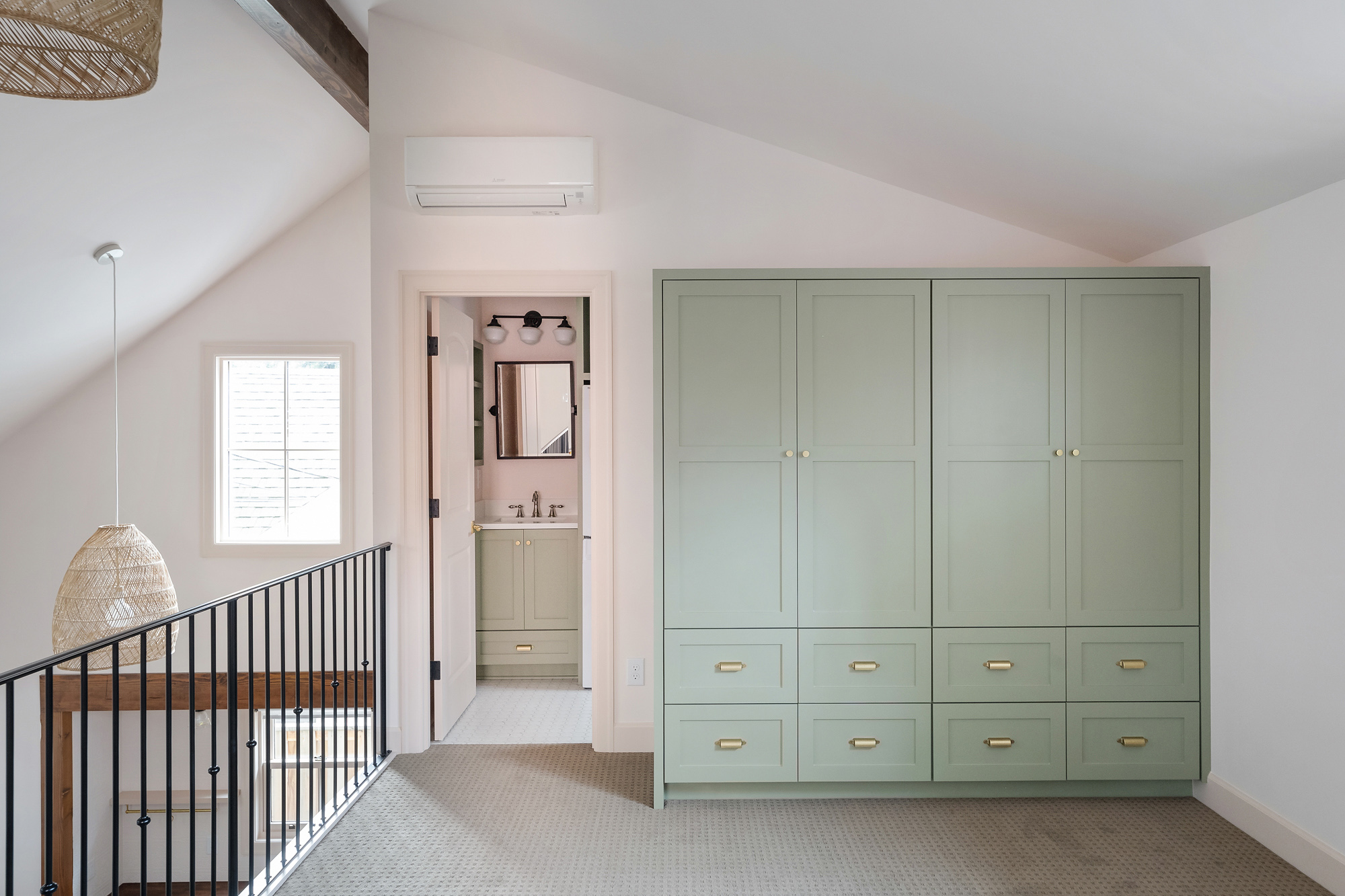 Loft bedroom with floor-to-ceiling green built-in wardrobe, sloped ceiling, and open door to the loft bathroom, Buckman ADU SE Portland by Tweto Architecture