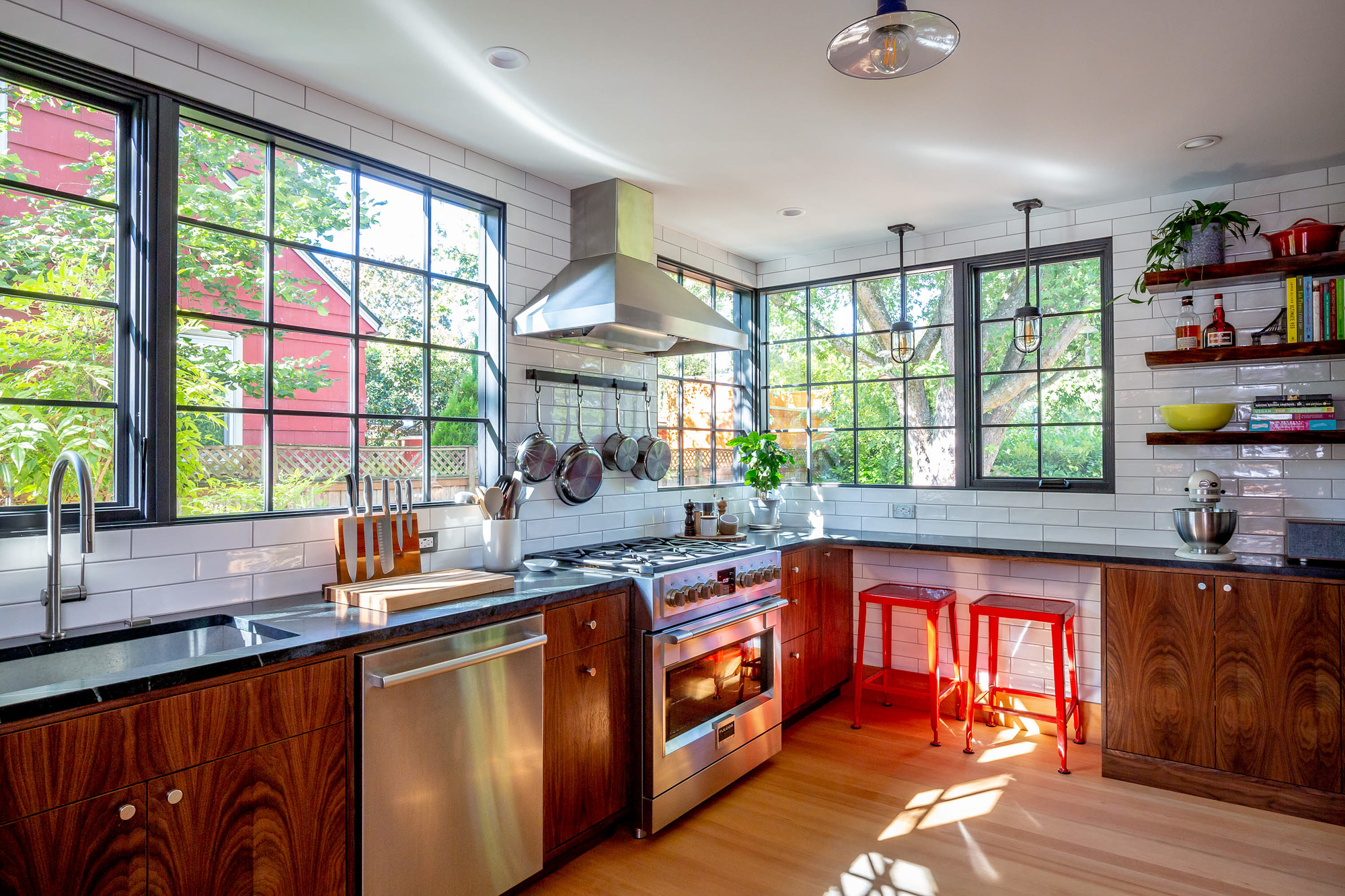 Full kitchen view with tall black-framed windows wrapping the corner, commercial range, walnut cabinets, and soapstone counters, Concordia Kitchen by Tweto Architecture, NE Portland