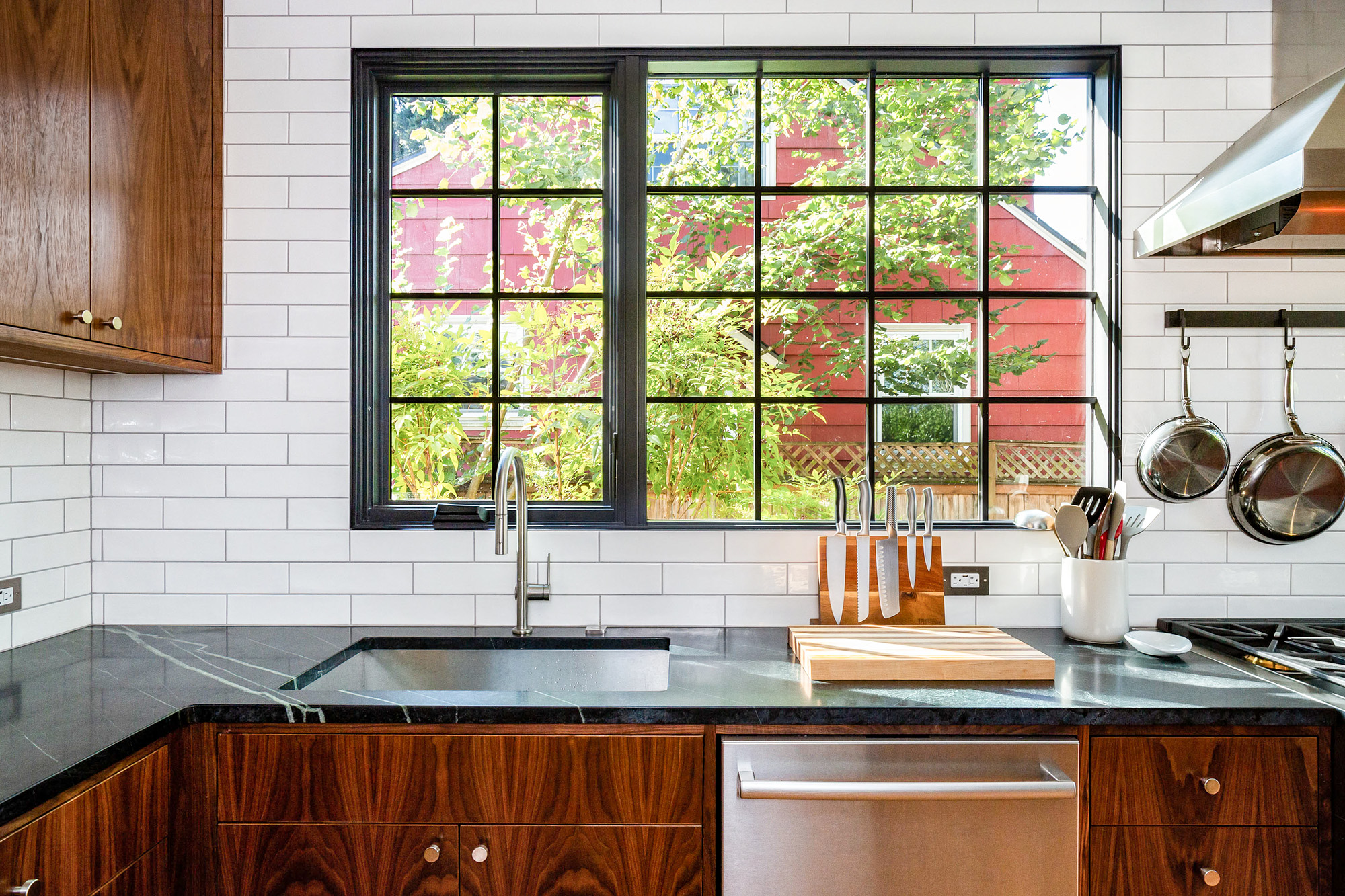 Sink counter with soapstone top and large black-framed window looking into the backyard, Concordia Kitchen by Tweto Architecture