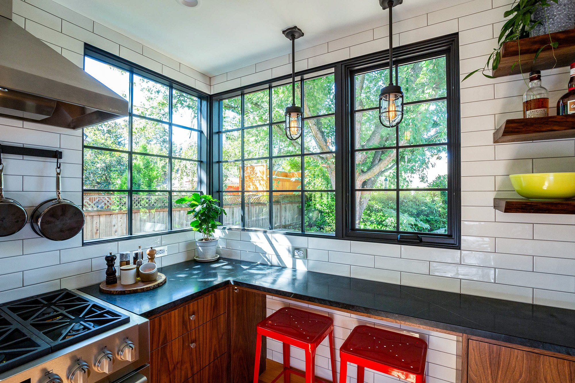 Corner where two runs of tall black-framed windows meet above the soapstone counter, with range and industrial pendant lights beyond, Concordia Kitchen by Tweto Architecture