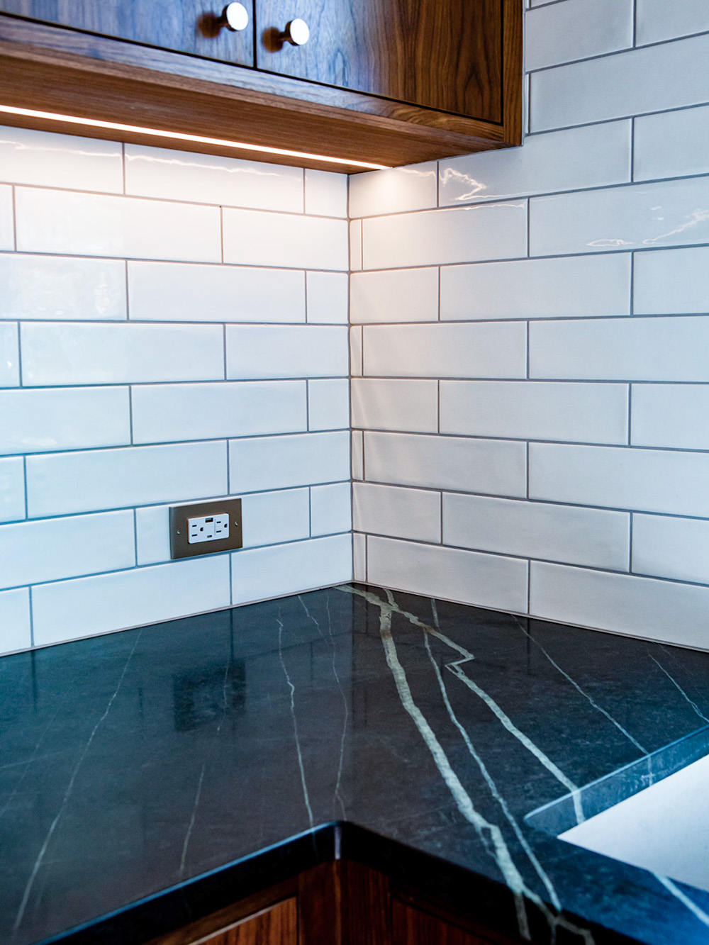 Close-up of soapstone counter corner showing veining and texture against white subway tile backsplash and walnut upper cabinet, Concordia Kitchen by Tweto Architecture