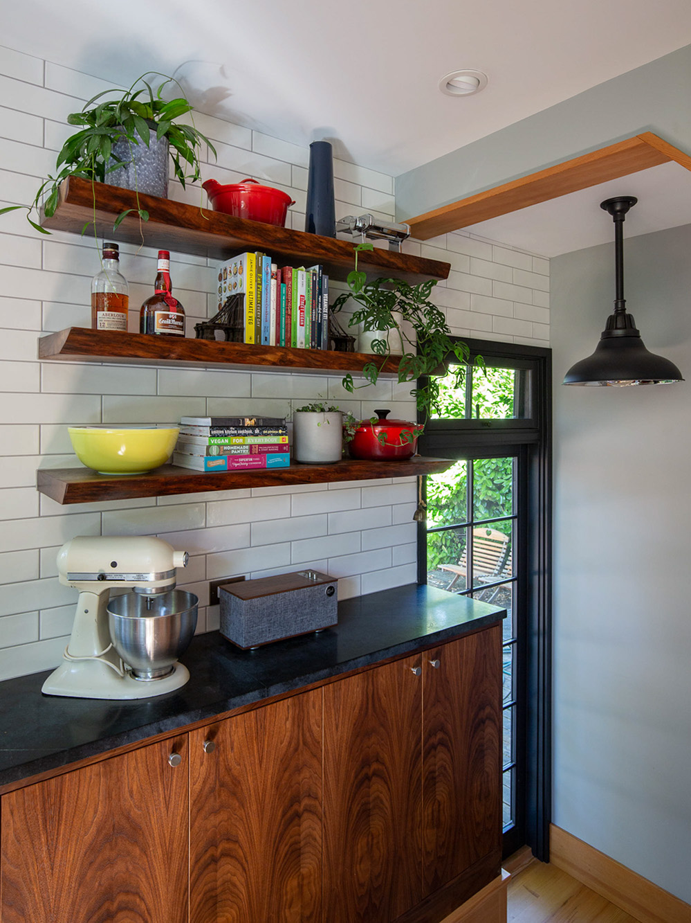 Open walnut floating shelves beside the black-framed door to the back deck, with stand mixer on the counter below, Concordia Kitchen by Tweto Architecture
