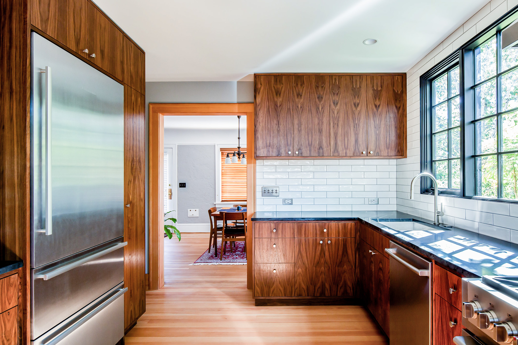 Walnut kitchen cabinets and stainless refrigerator with the open passage to the dining room visible beyond, Concordia Kitchen by Tweto Architecture