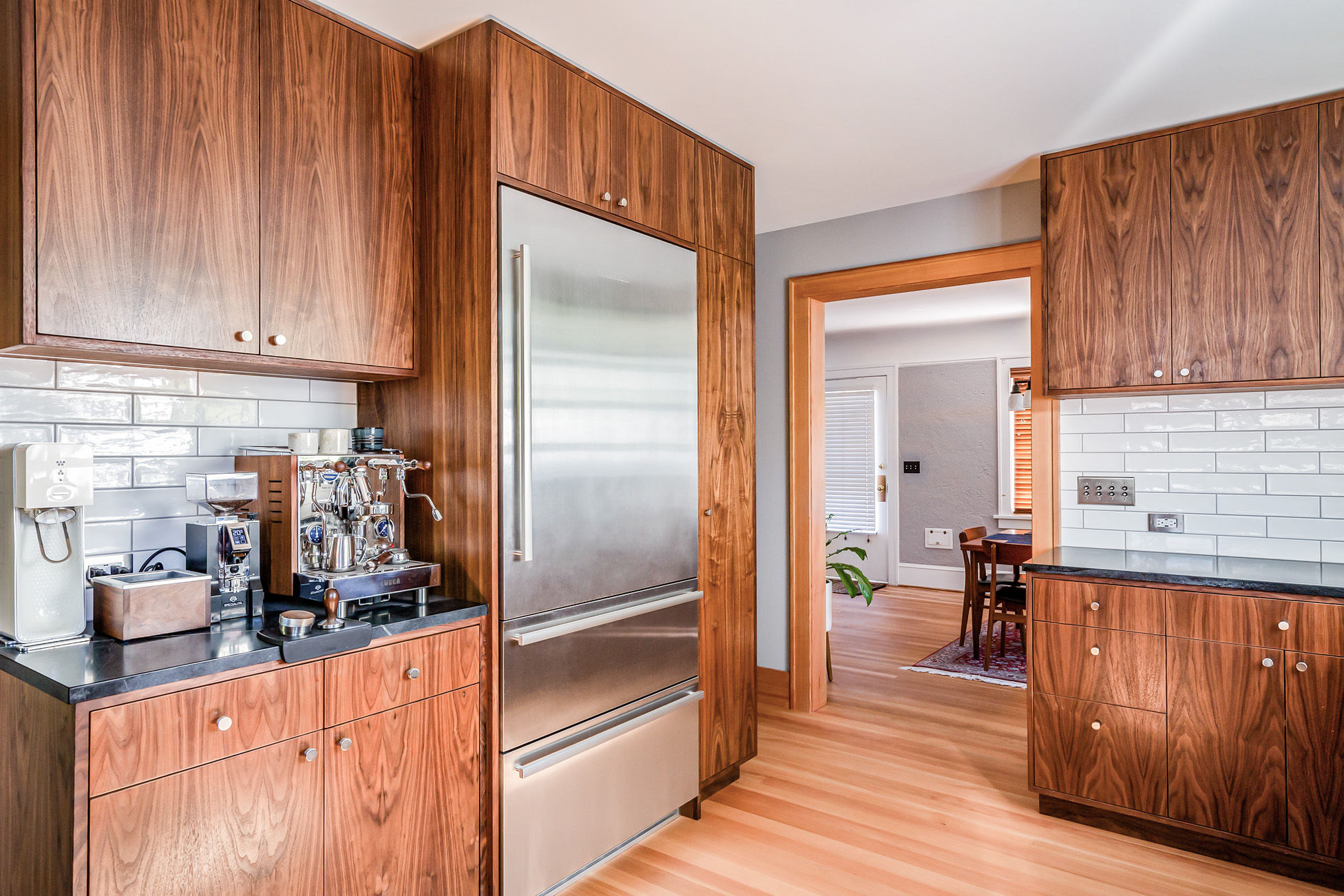 Coffee station and stainless refrigerator flanked by walnut cabinetry, with passage to dining room in the background, Concordia Kitchen by Tweto Architecture