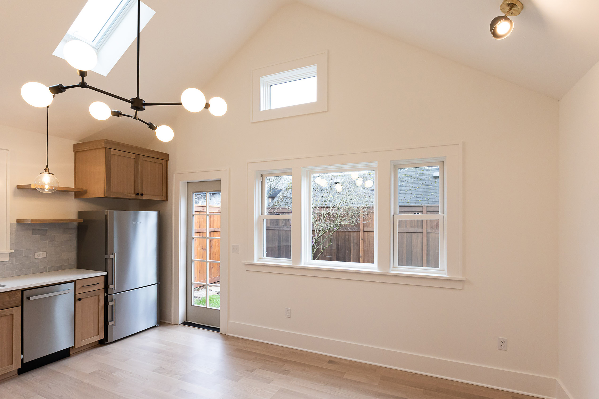 Vaulted great room with skylight, south-facing windows, globe pendant chandelier, and kitchen at left, Irvington ADU by Tweto Architecture