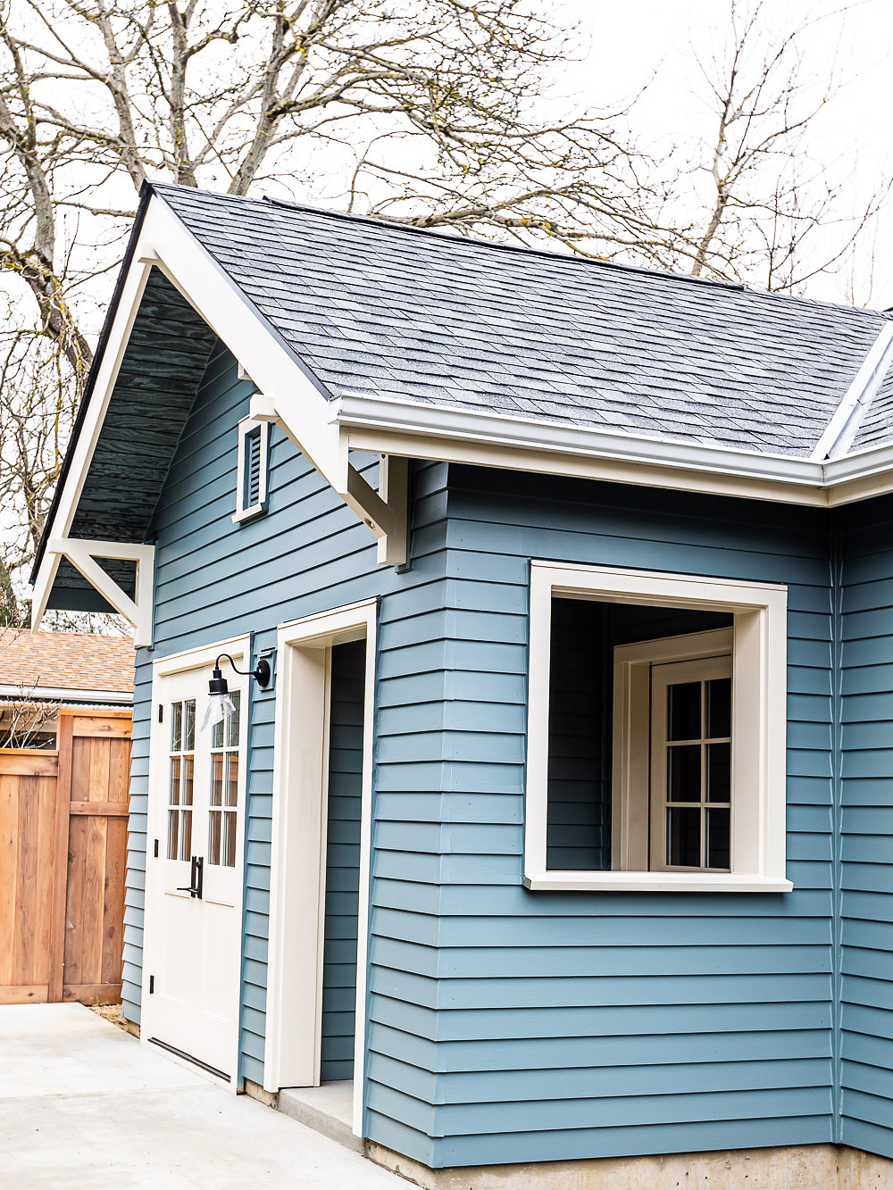 Corner exterior view showing craftsman gable brackets, covered entry porch with French doors and wall sconce, blue-grey lap siding, Irvington ADU by Tweto Architecture
