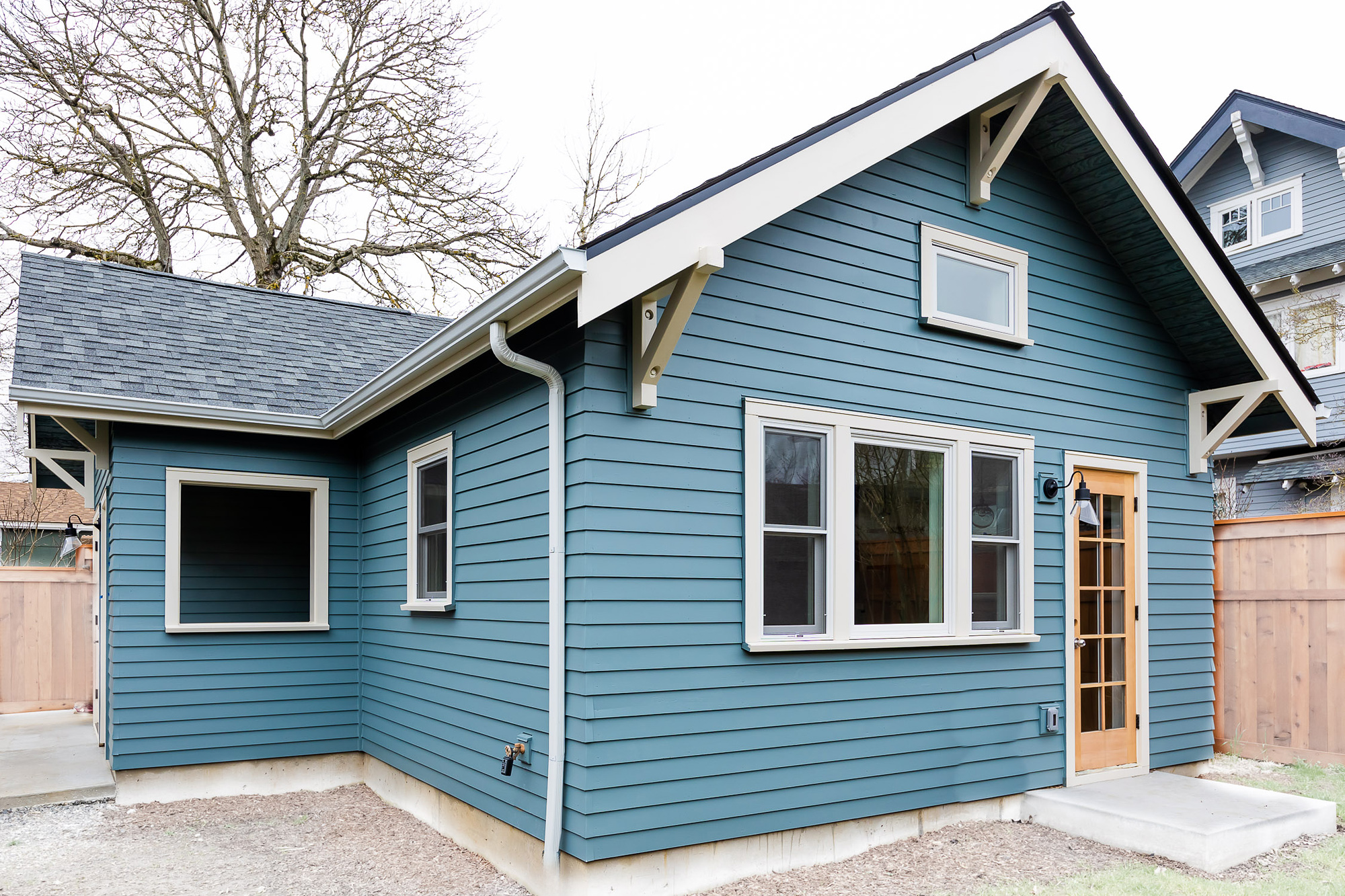 Rear and side exterior showing blue-grey craftsman siding, white trim details, and wood entry door, Irvington ADU by Tweto Architecture