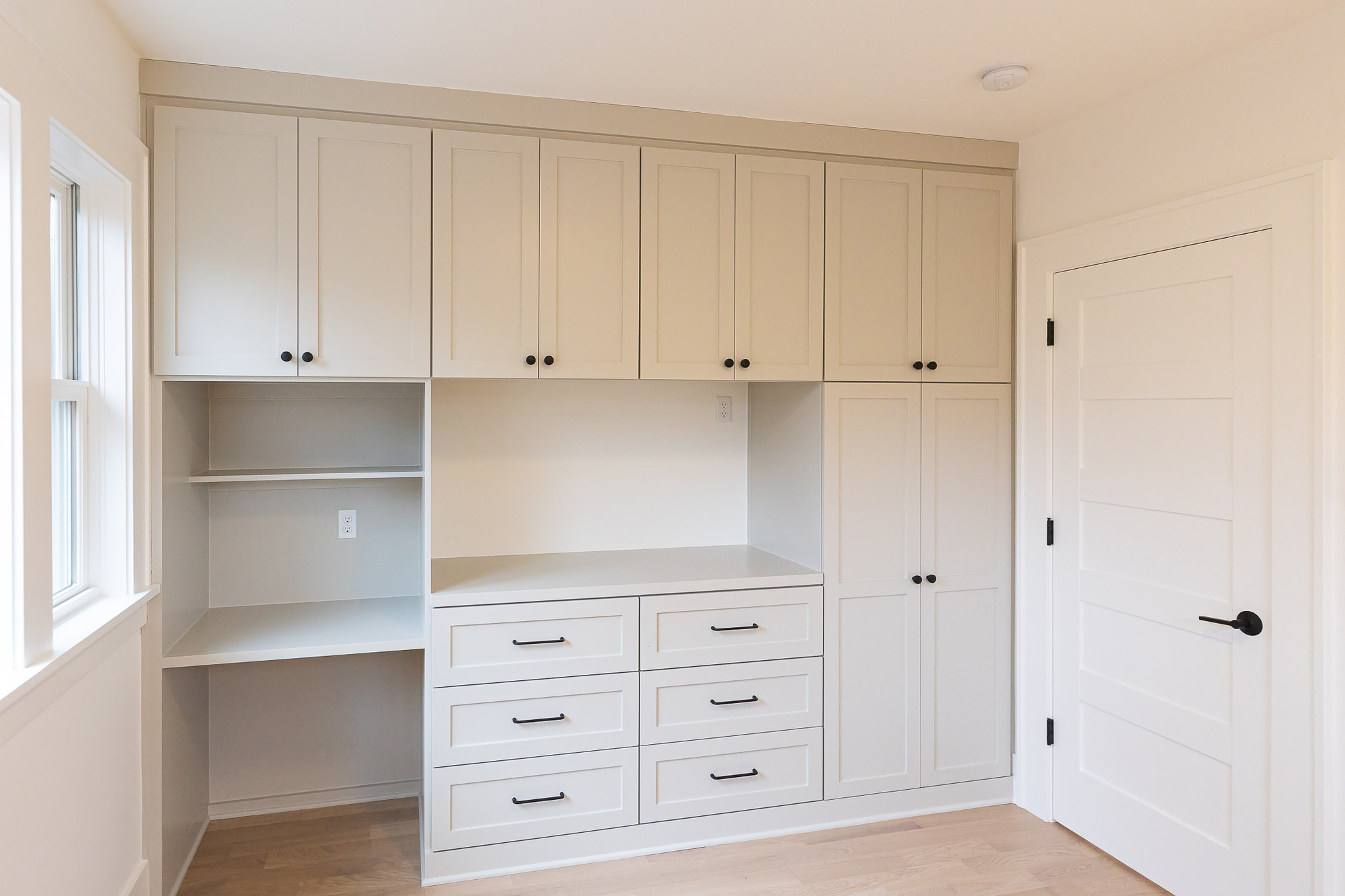 Bedroom with floor-to-ceiling white built-in wardrobe, upper cabinets, integrated desk with open shelf, and drawers with black hardware, Irvington ADU by Tweto Architecture