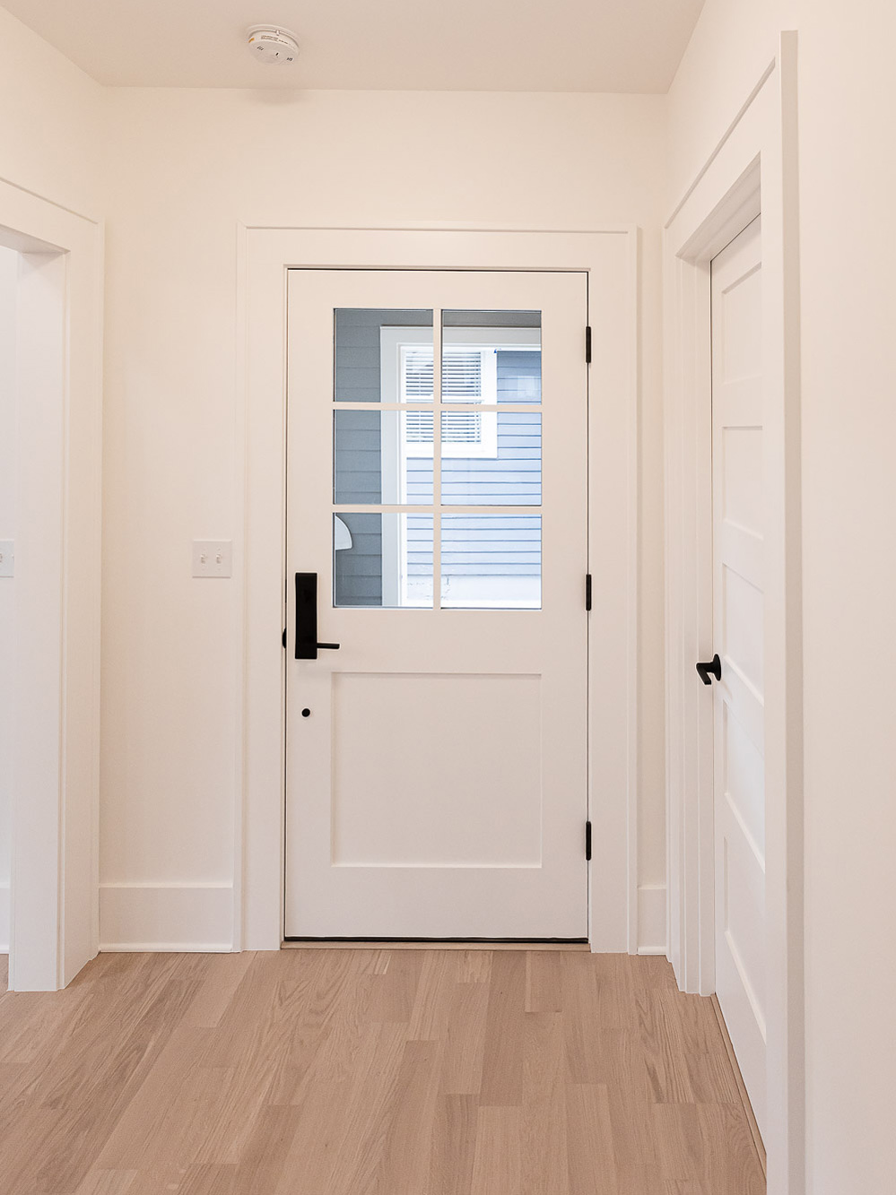 Entry hall with white craftsman door with six-light grille and black hardware, oak hardwood floor, bathroom and bedroom doors beyond, Irvington ADU by Tweto Architecture