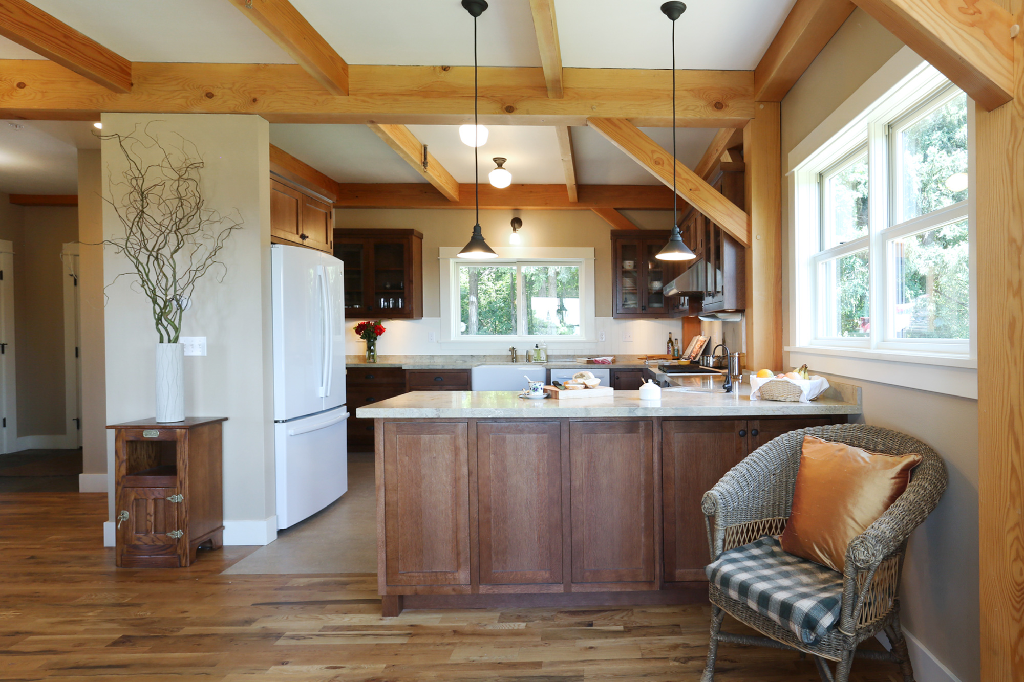 Kitchen with walnut shaker cabinets, marble island, pendant lights, and exposed Douglas Fir timber frame overhead, North Plains Timber Frame by Tweto Architecture