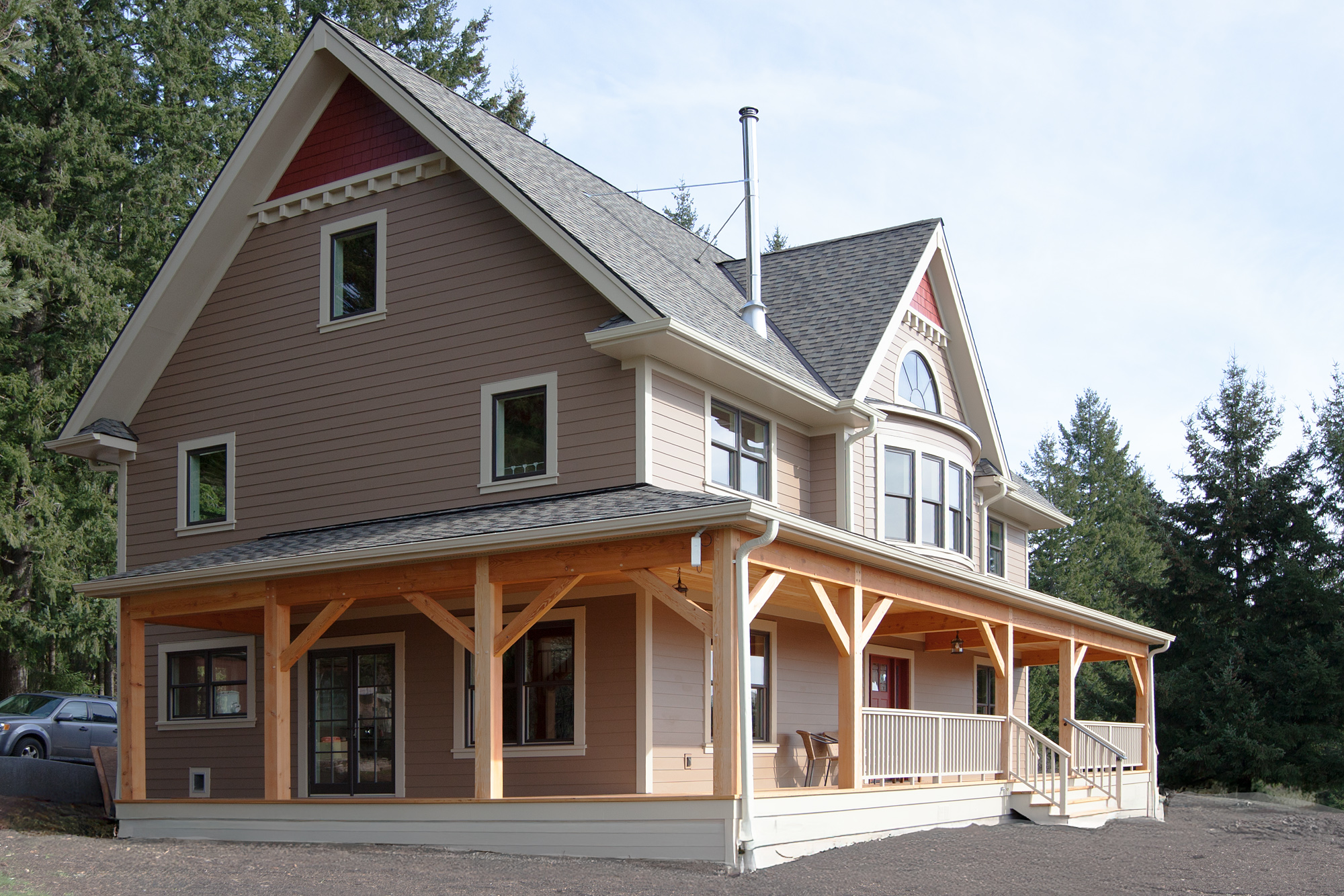 Corner view of farmhouse exterior showing west and south elevations with exposed timber porch columns and wraparound porch deck, North Plains Timber Frame by Tweto Architecture