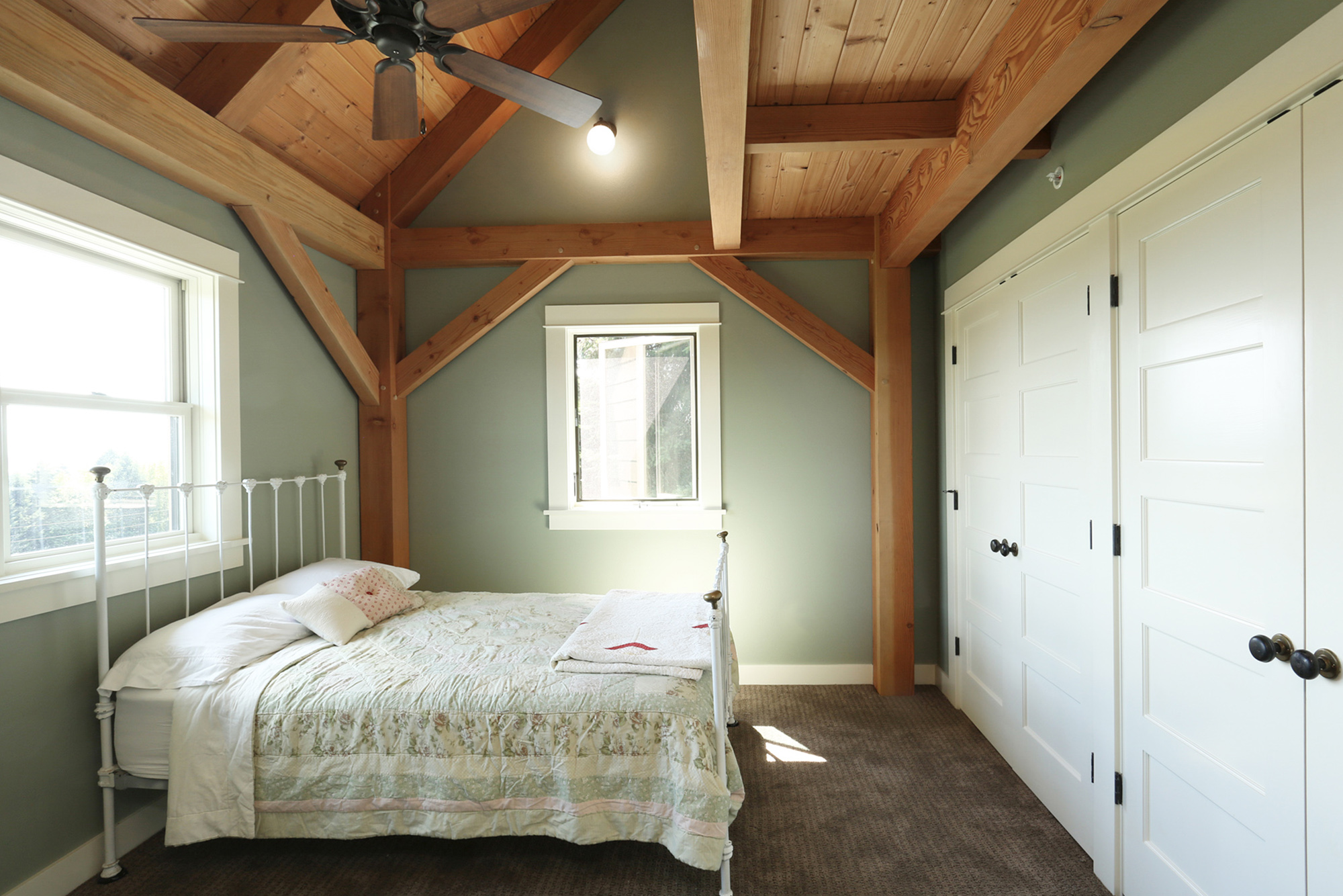 Second floor bedroom with vaulted ceiling, exposed timber knee brace, sage green walls, and white painted closet doors, North Plains Timber Frame by Tweto Architecture