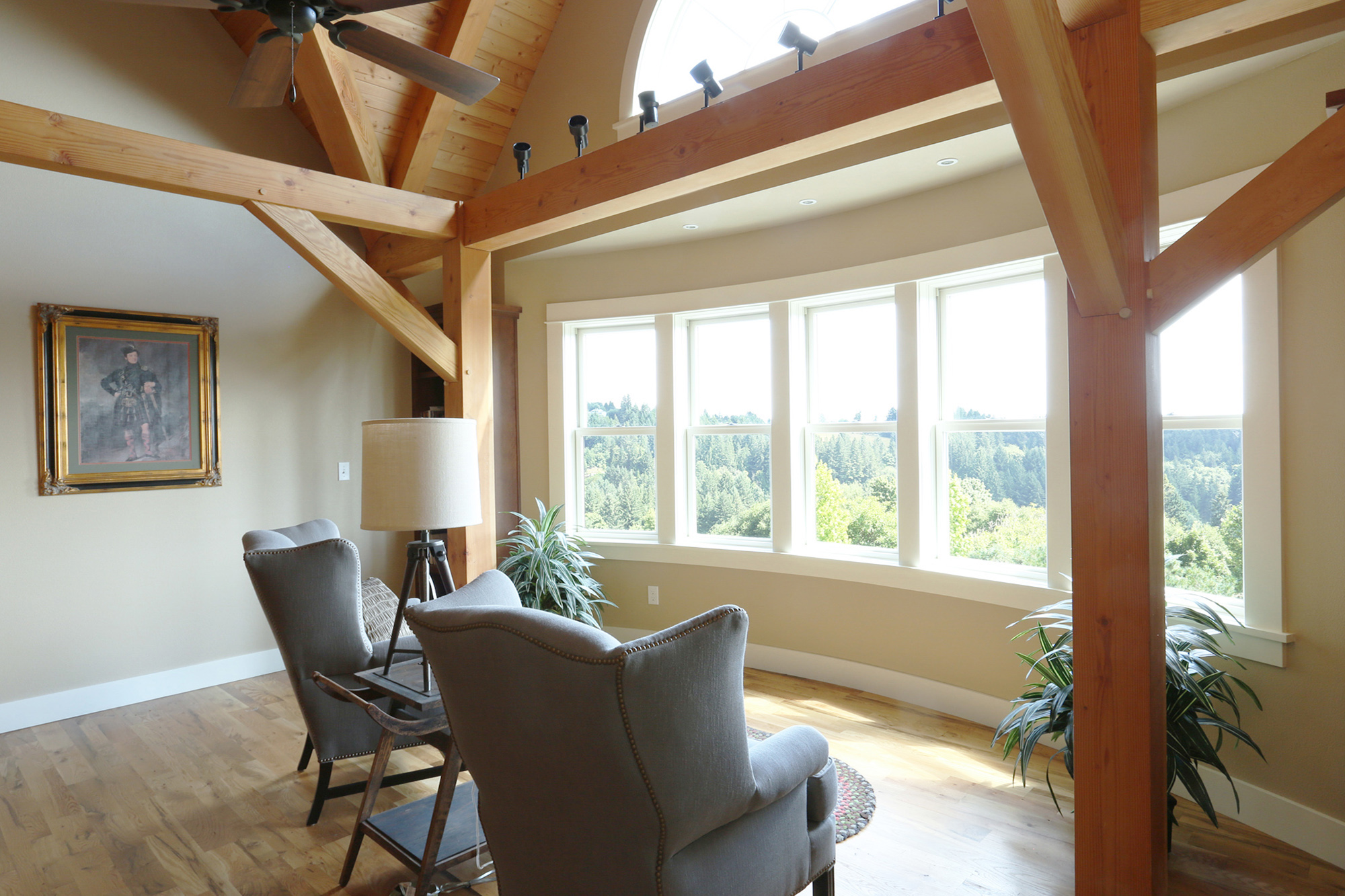 Second floor family room with curved south window bank and sweeping views over treetops, exposed timber frame and vaulted ceiling, North Plains Timber Frame by Tweto Architecture
