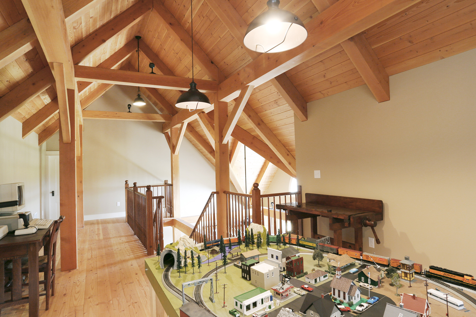 Loft hobby space with model train layout, exposed timber frame and Douglas Fir decking ceiling, open railing to second floor below, North Plains Timber Frame by Tweto Architecture