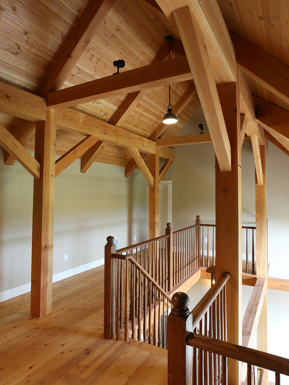 View from loft landing looking down open stair with exposed timber frame knee braces and Douglas Fir decking ceiling overhead, North Plains Timber Frame by Tweto Architecture