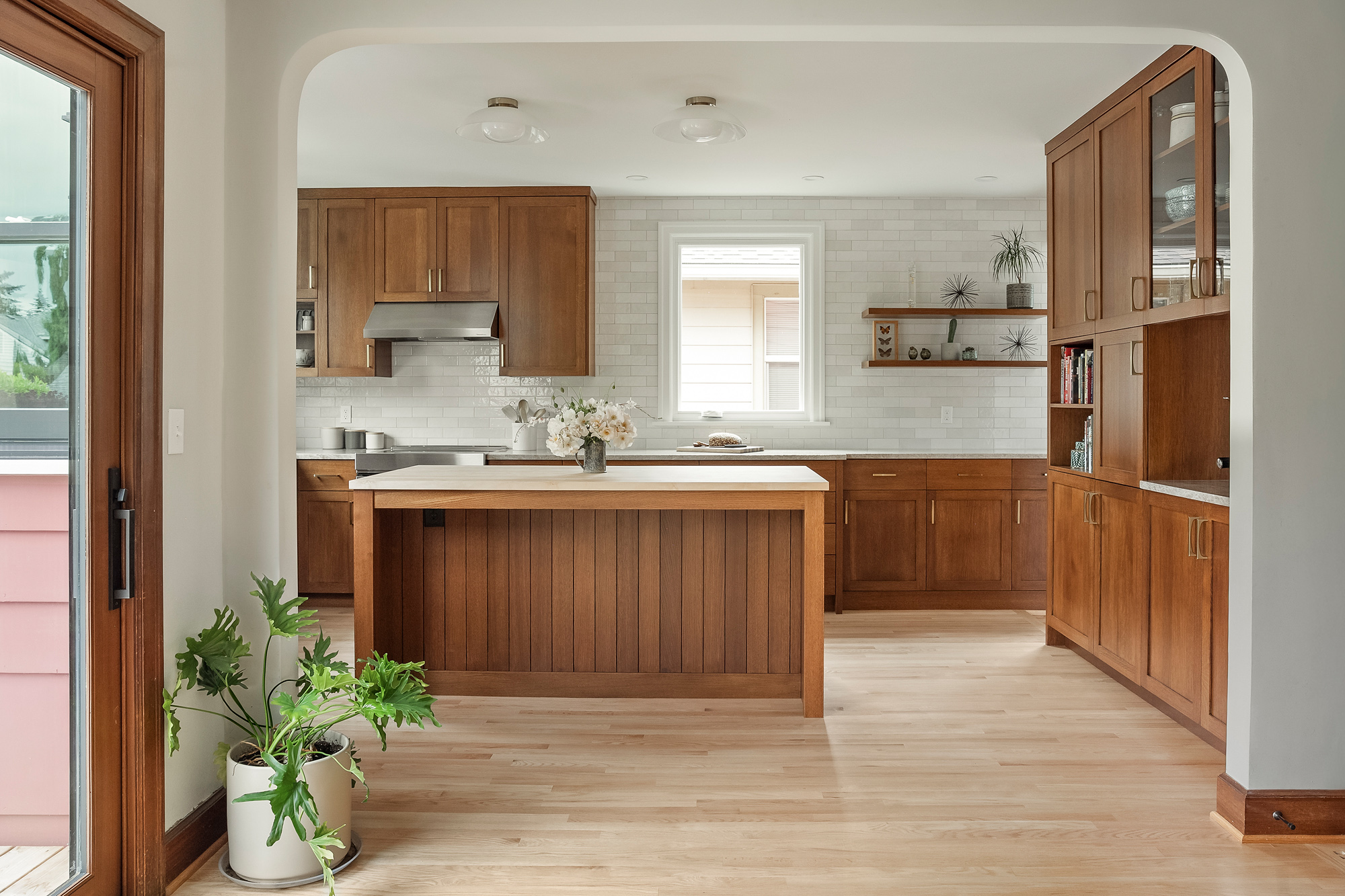 Kitchen seen through the widened dining room opening, with white oak island, range wall, and tall glass-front cabinets, Rose City Kitchen by Tweto Architecture