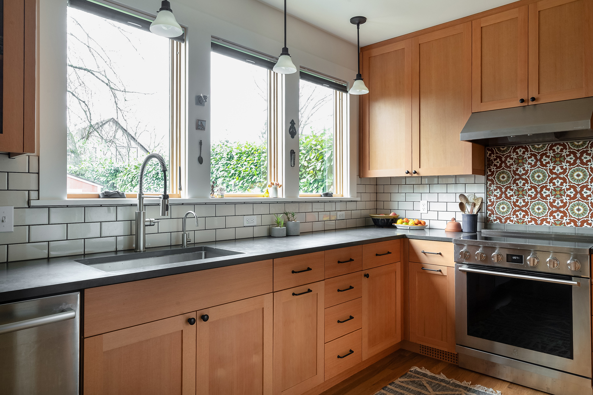 Sink wall with three east-facing windows, dark quartz countertop and vertical grain Douglas Fir cabinets, Sabin Kitchen remodel by Tweto Architecture, NE Portland