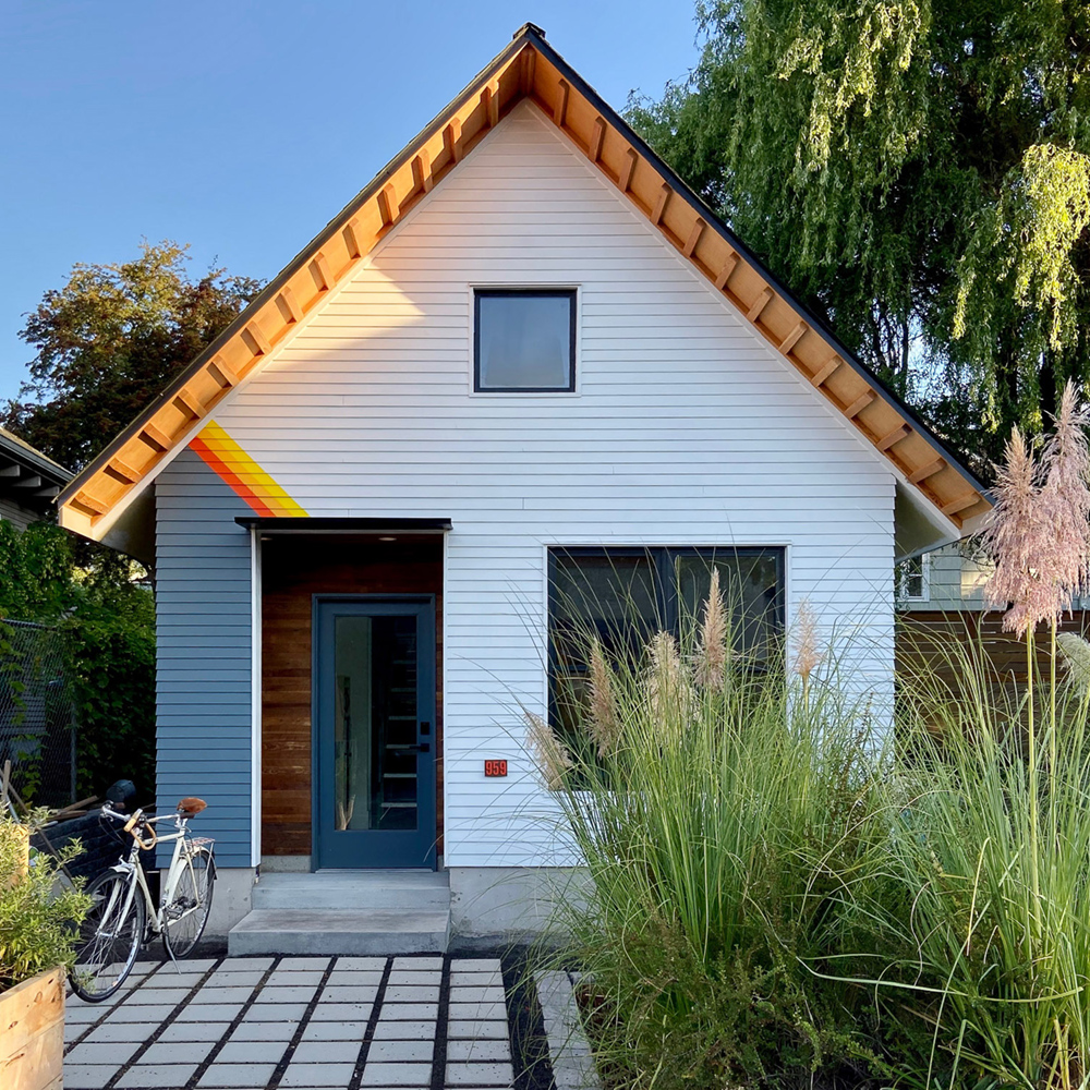 ADU exterior with white lap siding, gable roof, blue entry door, and ornamental grasses, by Tweto Architecture Portland
