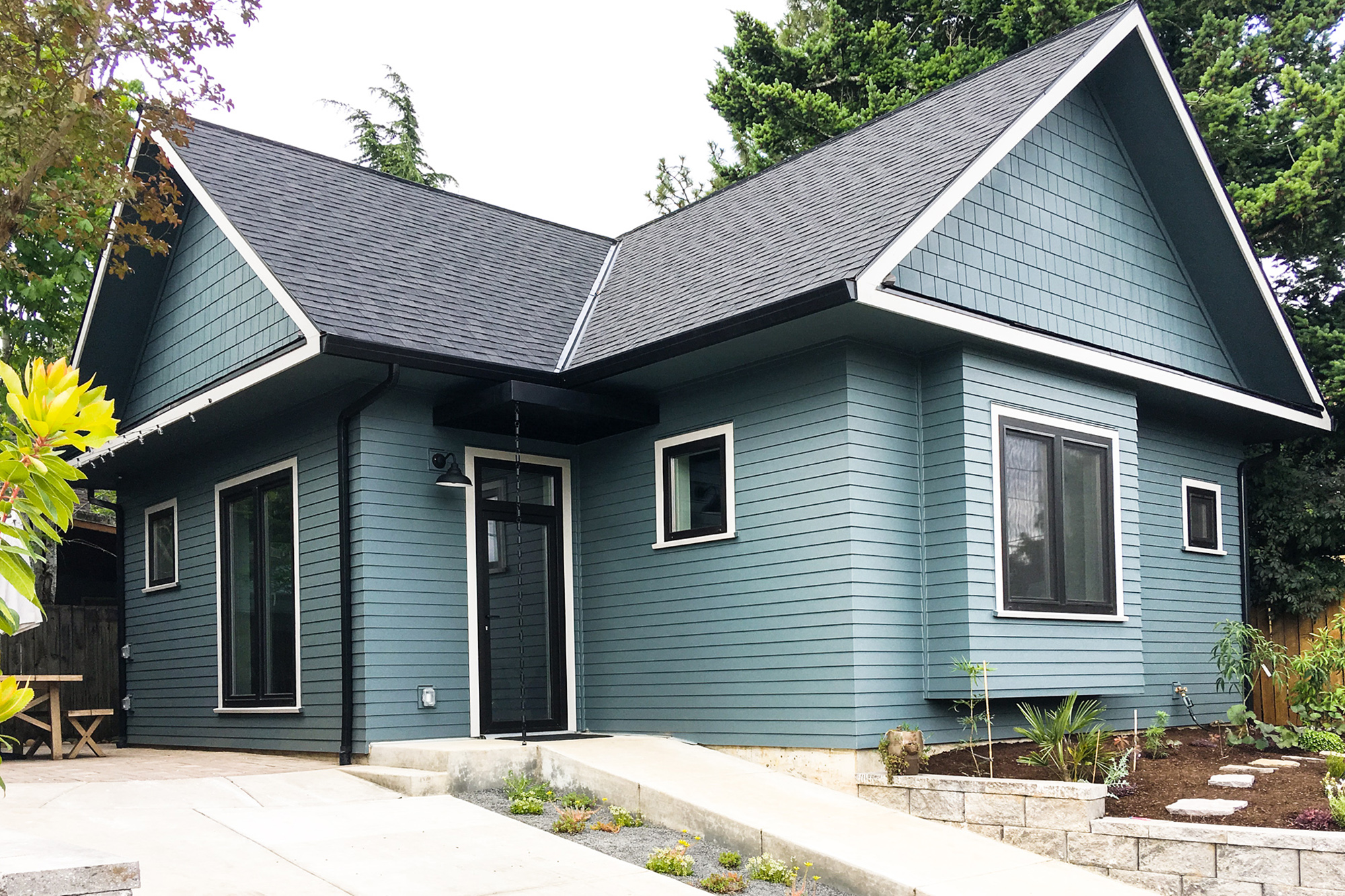 Front exterior of the Siskiyou Street Recording Studio, a blue-green accessory structure with dark trim, gable roof, covered entry, and new landscaping with stone retaining wall, Beaumont neighborhood Portland, by Tweto Architecture