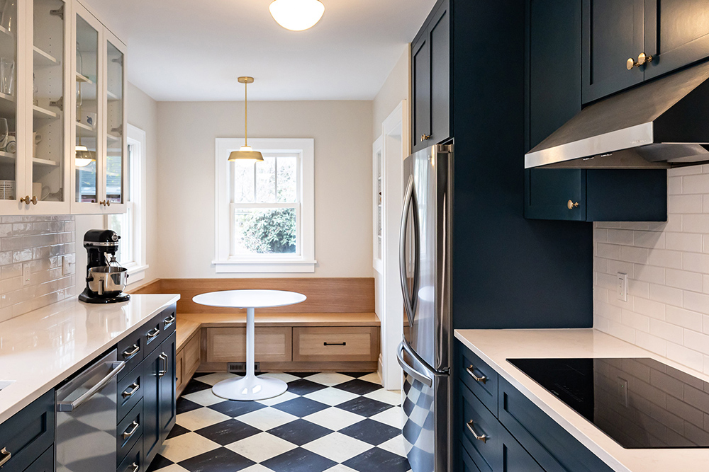 Galley kitchen with navy shaker cabinets, checkerboard linoleum floor, and white oak breakfast nook, Stanton Street Kitchen remodel by Tweto Architecture
