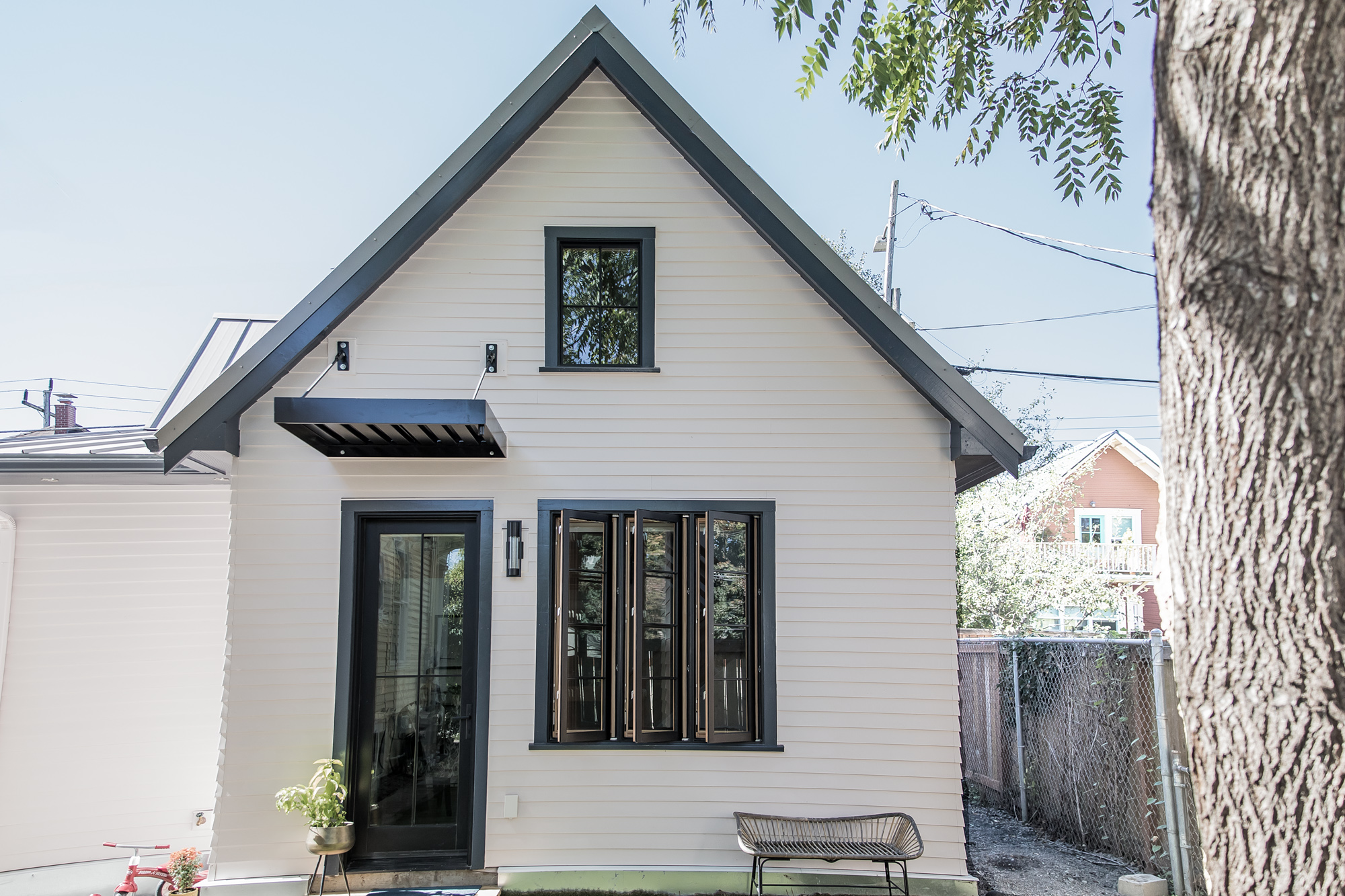Rear exterior of the Vancouver Avenue ADU, white lap siding with dark trim, gable roof, large folding wood-framed windows opening to the private yard, Vancouver Avenue ADU by Tweto Architecture